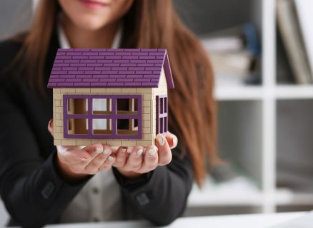 Businesswoman in the office holds a miniature toy house in her hand the subject of real estate services sales of renting the construction of apartments and housing for families